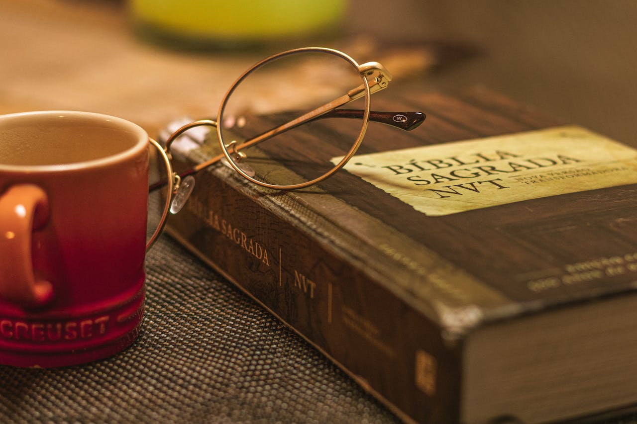 A Biblia Sagrada with glasses rests on a table beside a red mug, symbolizing relaxation and reflection.